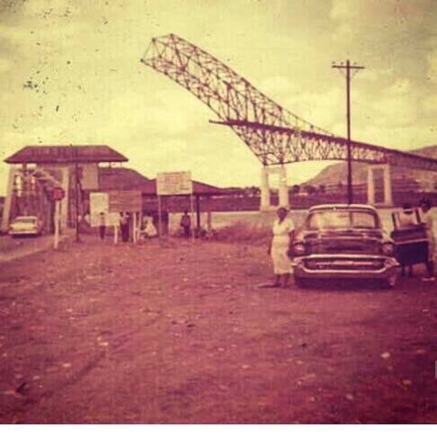 Vintage photo showing the construction of the Bridge of the Americas in Panama. The old bridge structure is visible with a classic car and people in the foreground. Image courtesy of knowpanama.link intellectual property.